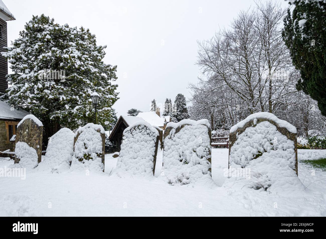 Grabsteine in einem mit Schnee bedeckten Kirchhof im Winter, Großbritannien. Winterliche Szene. Stockfoto