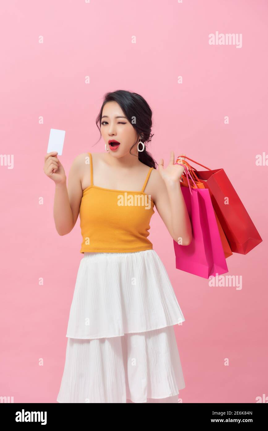 In voller Länge Porträt eines glücklichen schönen Mädchen trägt Kleid Und Einkaufstaschen halten und Kreditkarte abgesondert zeigen Rosa Hintergrund Stockfoto