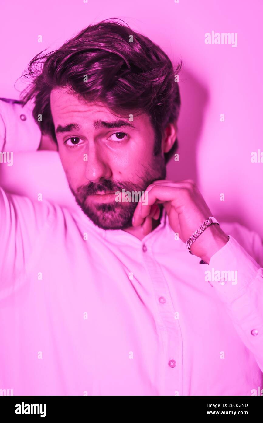 Süßer Look eines kaukasischen Mannes in einem weißen Hemd, beleuchtet mit einem rosa Neonlicht Stockfoto