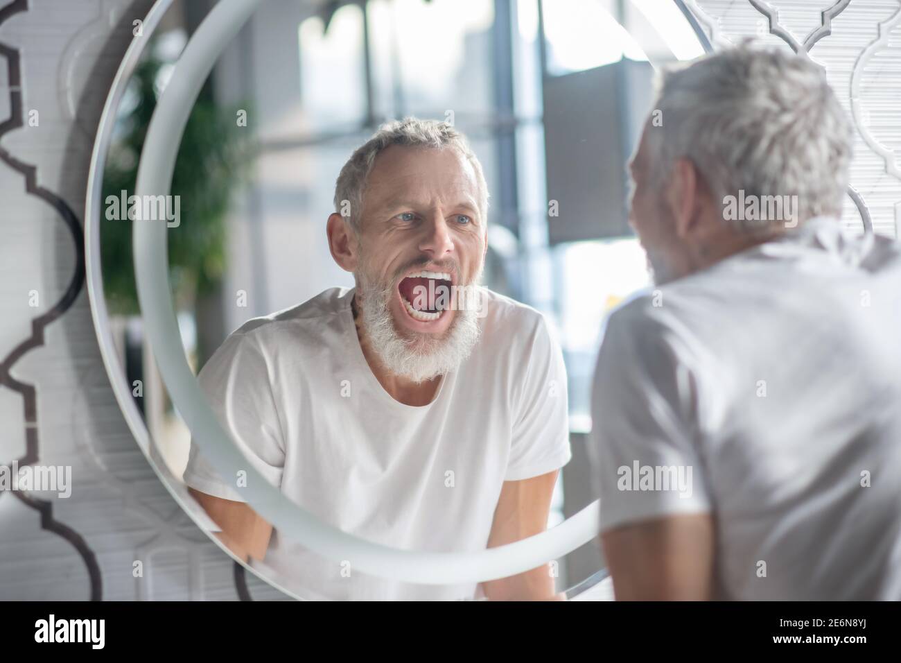 Mann macht lustige Gesichter in der Nähe des Spiegels Stockfoto