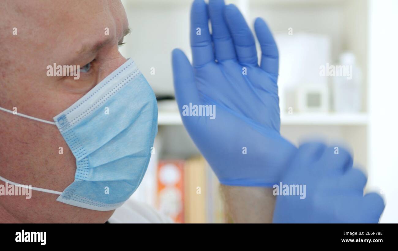 Arzt trägt eine schützende Gesichtsmaske und legt OP-Handschuhe auf seine Hände. Stockfoto