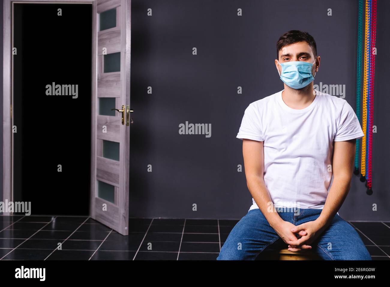 Kaukasischer Mann, der in einem Büro sitzt und eine medizinische Maske trägt und auf die Schlange für einen Impfstoff wartet. Massenimpfung der Angestellten auf einem Bürohintergrund. Stockfoto