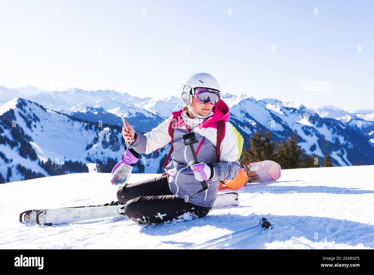 Mädchen auf Skiern sitzen auf Schnee. Immer bereit, ein selfy Foto zu machen. Stockfoto
