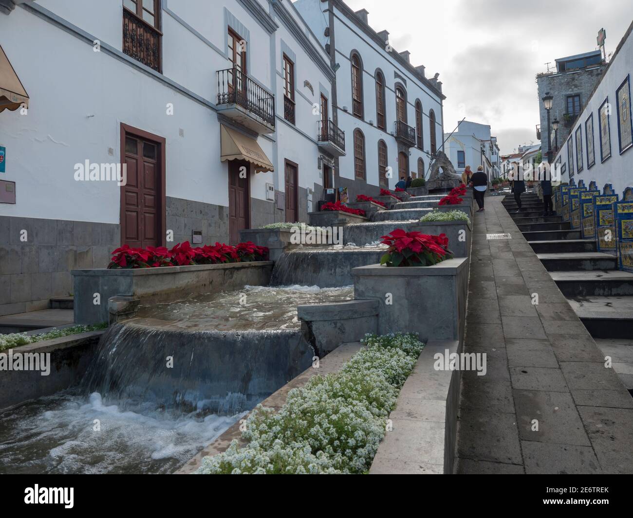 Firgas, Gran Canaria, Kanarische Inseln, Spanien 13. Dezember 2020: Blick auf die Straße Paseo de Gran Canaria mit Wasserfall Brunnen, Blumen und Keramik Stockfoto