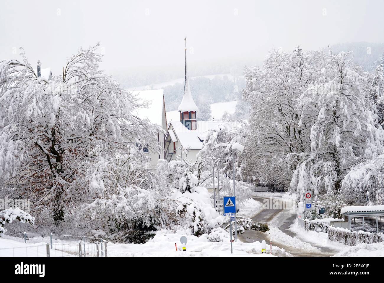 Altes reformiertes Kirchengebäude in Urdorf, Schweiz im Winter mit einer Straße und Kreuzung im Vordergrund, alle mit Schnee bedeckt nach extremem Schneefall Stockfoto