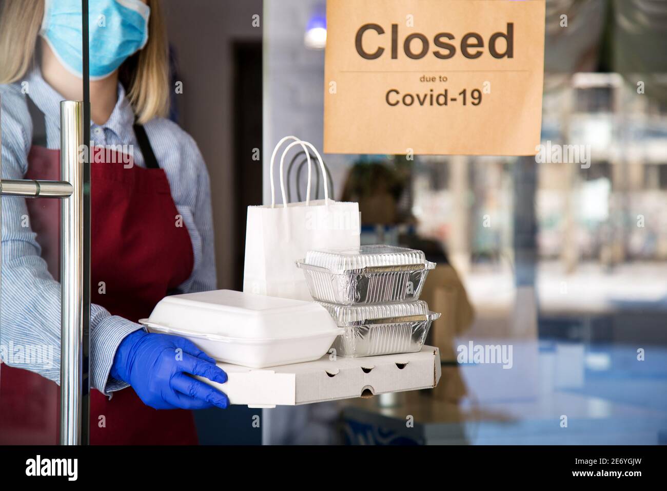 Kellnerin in schützender medizinischer Maske und Handschuhe arbeiten mit Take-away-Bestellungen. Der Kellner gab Essen zum Mitnehmen, während er absperrte, das Coronavirus wurde heruntergefahren. Essen Stockfoto