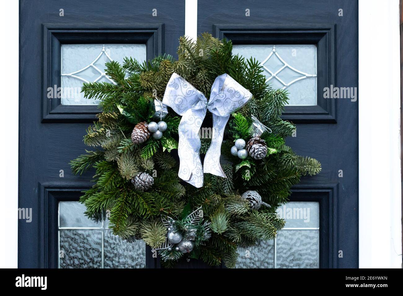 Weihnachtskranz mit großem weißen Band, das auf einem schwarzen hängt Vordertür mit großen Glaspaneelen Stockfoto
