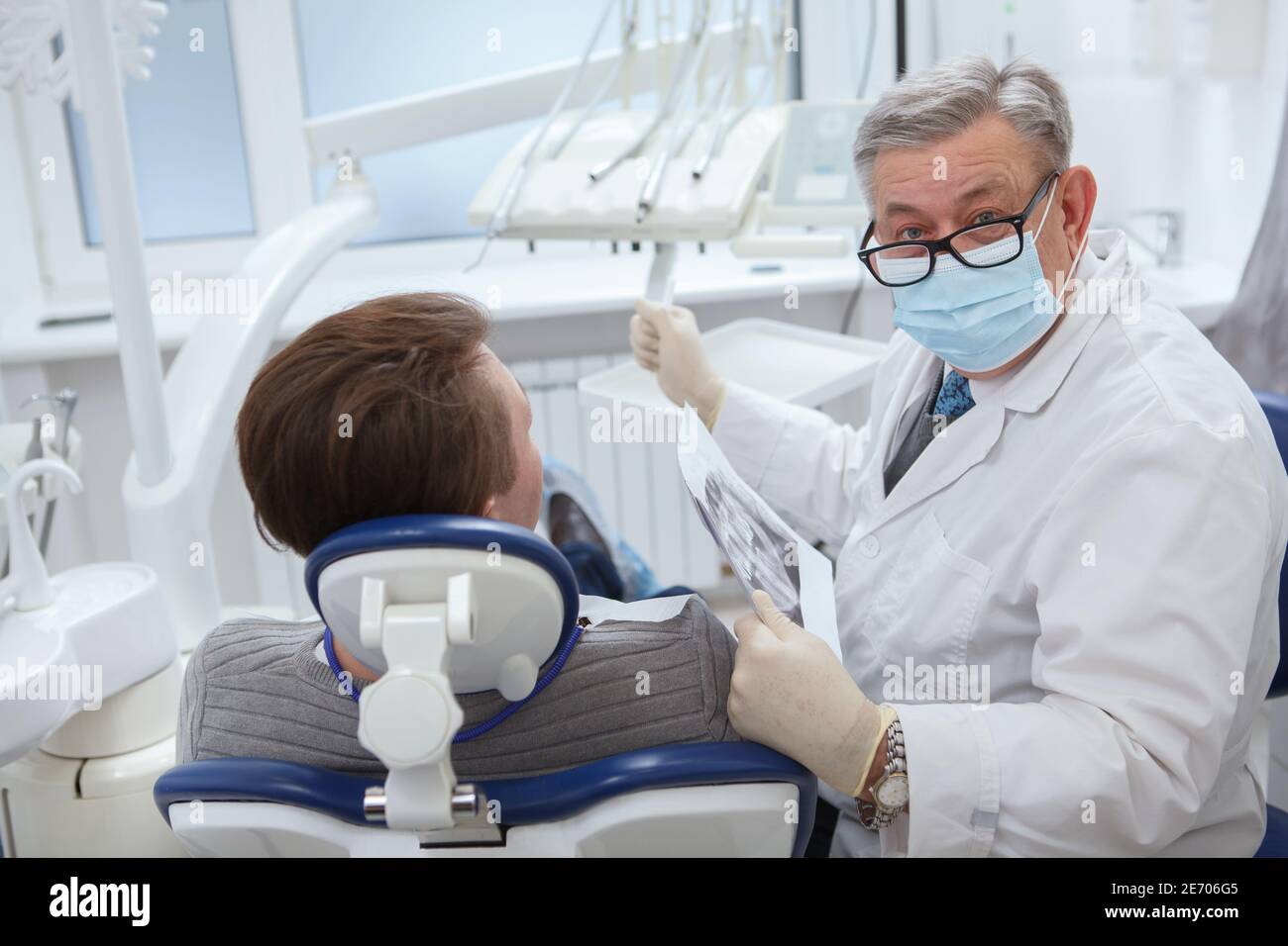 Senior männlichen Zahnarzt trägt medizinische Gesichtsmaske, Blick auf die Kamera während der zahnärztlichen Termin mit dem Patienten Stockfoto