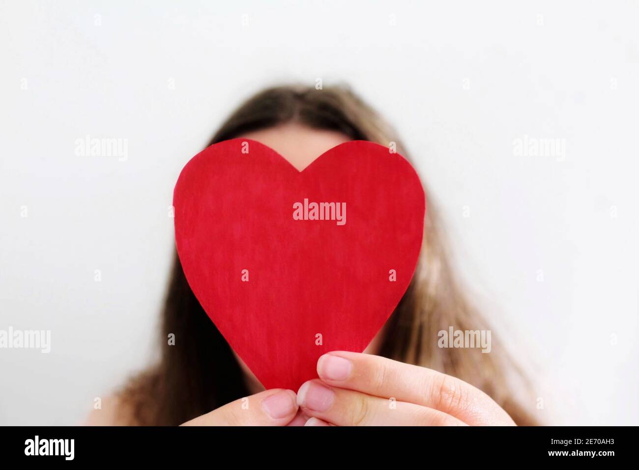 Eine weiße Frau mit braunen Haaren hält ein rotes Herz vor ihrem Gesicht und versteckt ihr Gesicht. Liebe, valentinstag und Blind Date Konzept. Stockfoto