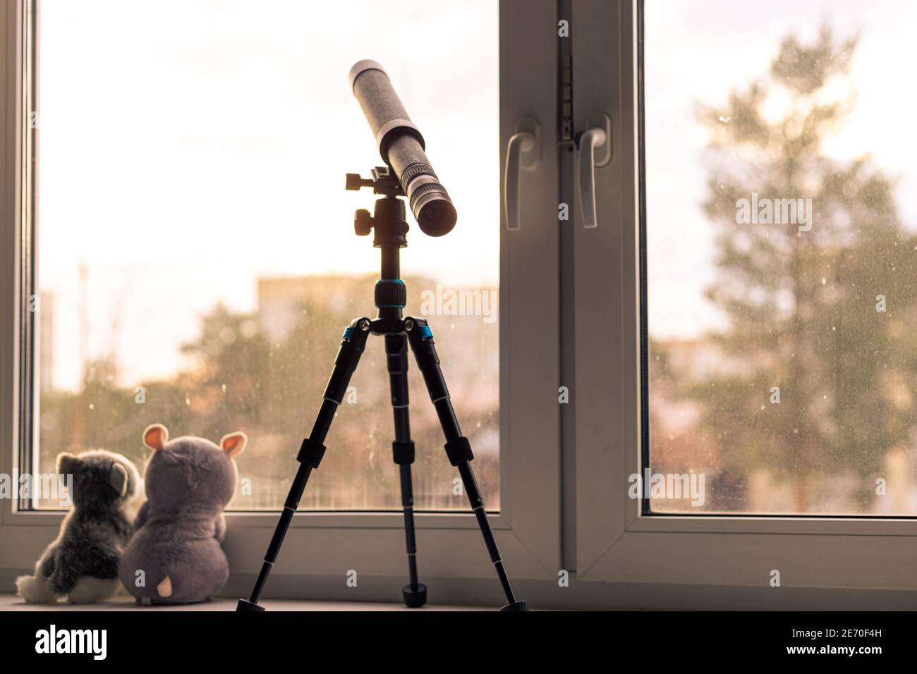 Auf der Fensterbank steht auf einem Stativ ein Teleskop in den Himmel gerichtet, neben zwei weichen Spielzeug auf die Straße gedreht sitzen, braun getönt, retro, selbst-i Stockfoto
