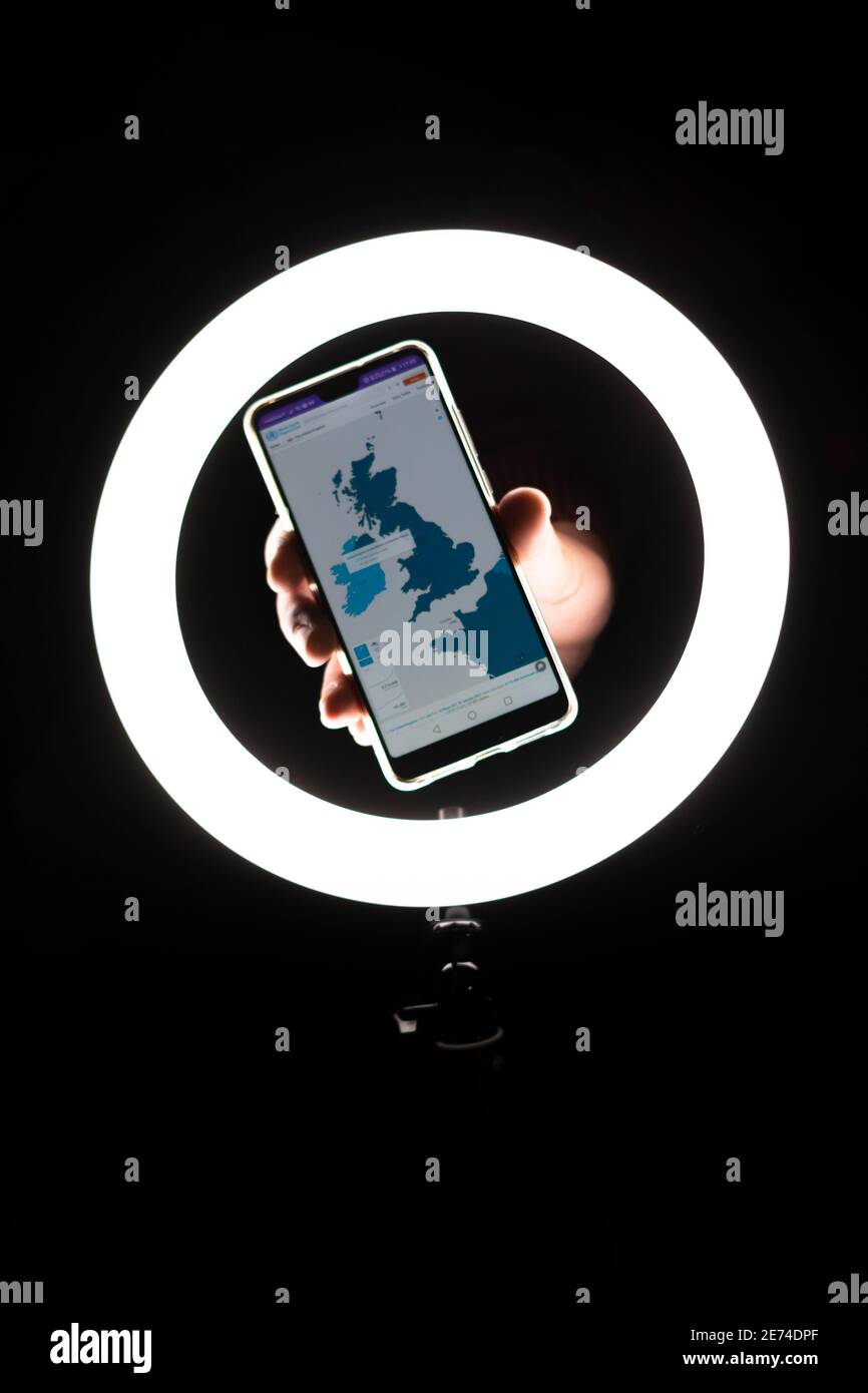 Anzeige von Mobiltelefonanwendungen mit Karte des vereinigten Königreichs in covid19-Zeiten mit Ringlichtbeleuchtung auf dem Hintergrund. Bereitstellungs-Apps oder -Jobs. Stockfoto