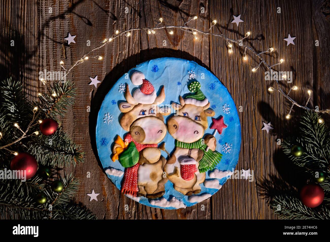Dekoriert Lebkuchen mit zwei Comic-Kuh-Figuren. Weihnachtliche Wohnung mit Tannenzweigen, roten Kugeln und Sternen Konfetti. Dunkle Holzbretter, Draufsicht Stockfoto
