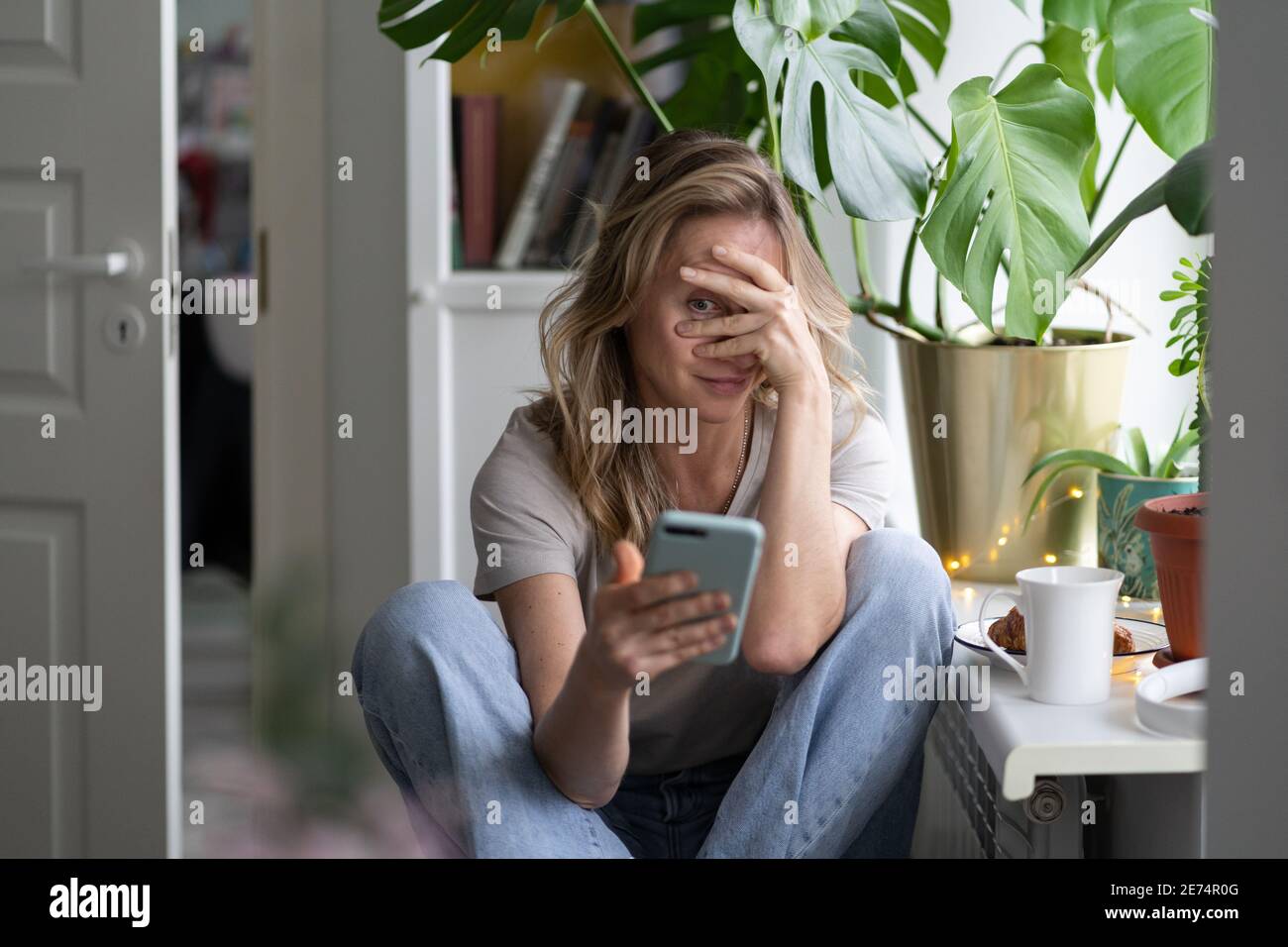 Schüchterne Frau, die im Videochat telefoniert, guckt durch ihre Hände, die ihr Gesicht bedecken Stockfoto