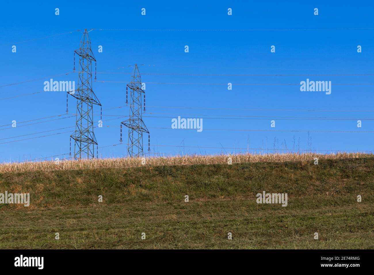 Kein Leben ohne Strom. Zwei große Strommasten hinter einem grünen Hügel in einem schönen wolkenlosen blauen Himmel, ohne Menschen am Tag Stockfoto