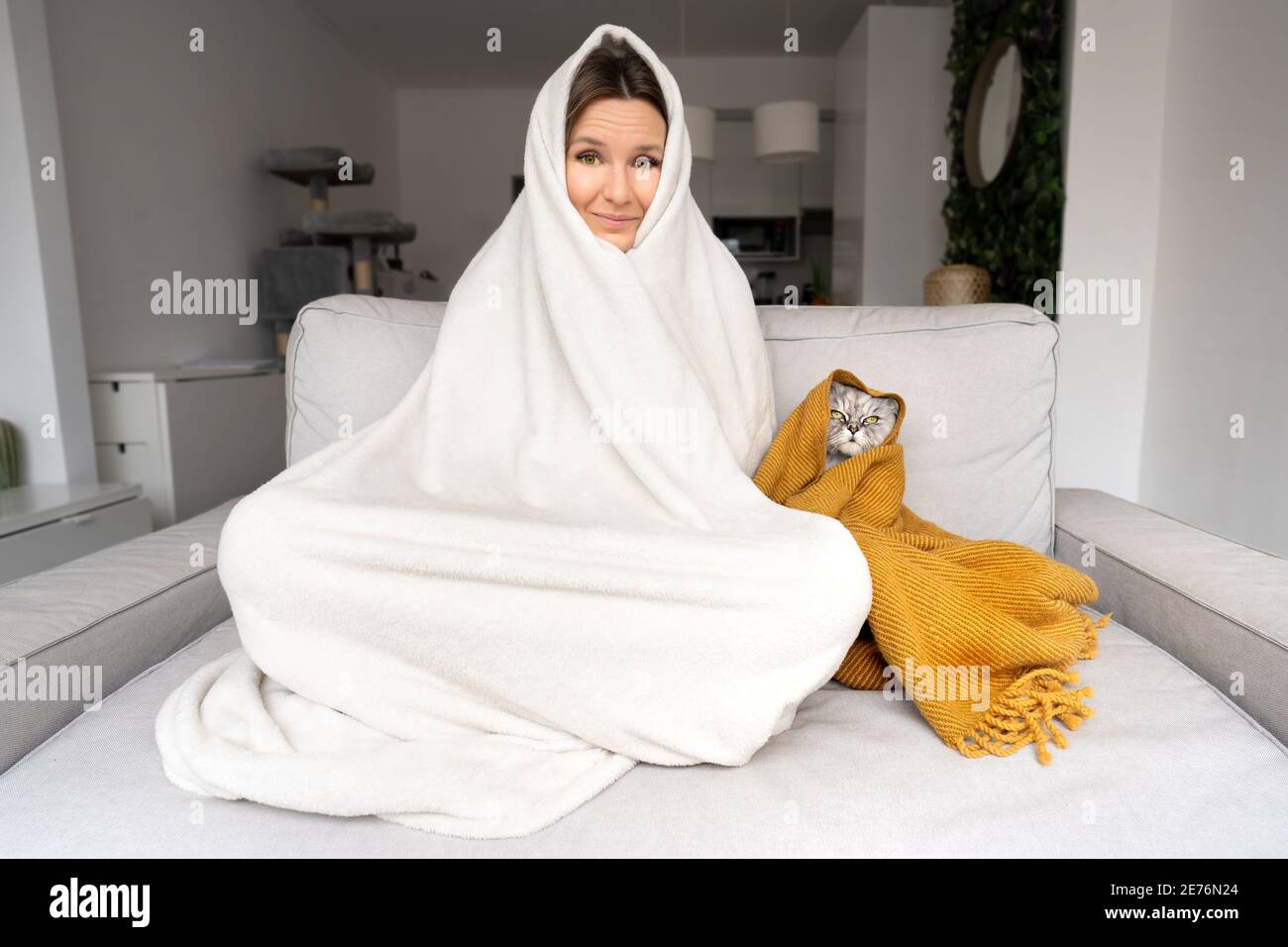 Eiskalte Frau und Katze unter einem Plaid haben Kälte an Das Sofa zu Hause Stockfoto