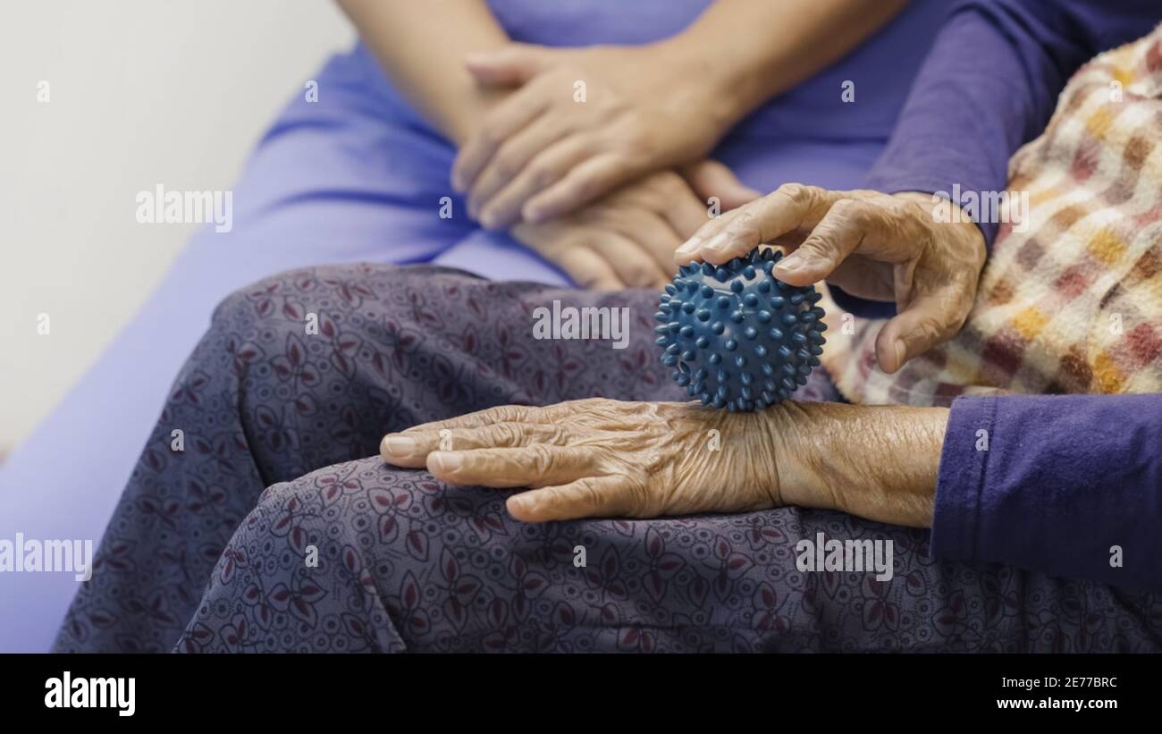 Ältere Frau tut Gummiball für Übung Finger, Handfläche, Hand-und Fußmuskel mit Betreuer kümmern. Stockfoto