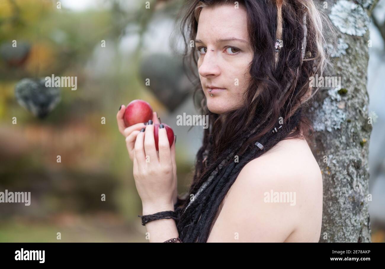 Schöne junge individuelle, exzentrische Frau, mit attraktiven Dreadlocks, Piercing und Tattoo zeigt im Garten Eden Aufruf für den Apfel von te Stockfoto