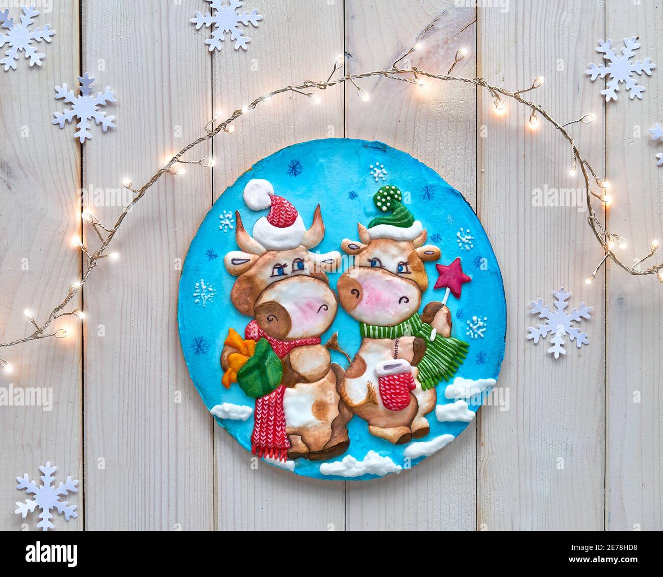 Dekoriert Lebkuchen mit zwei Comic-Kuh-Figuren. Weihnachten flach lag mit festlichen Lichtern Girlande und Schneeflocken. Aus weißen Holzplanken, oben Stockfoto