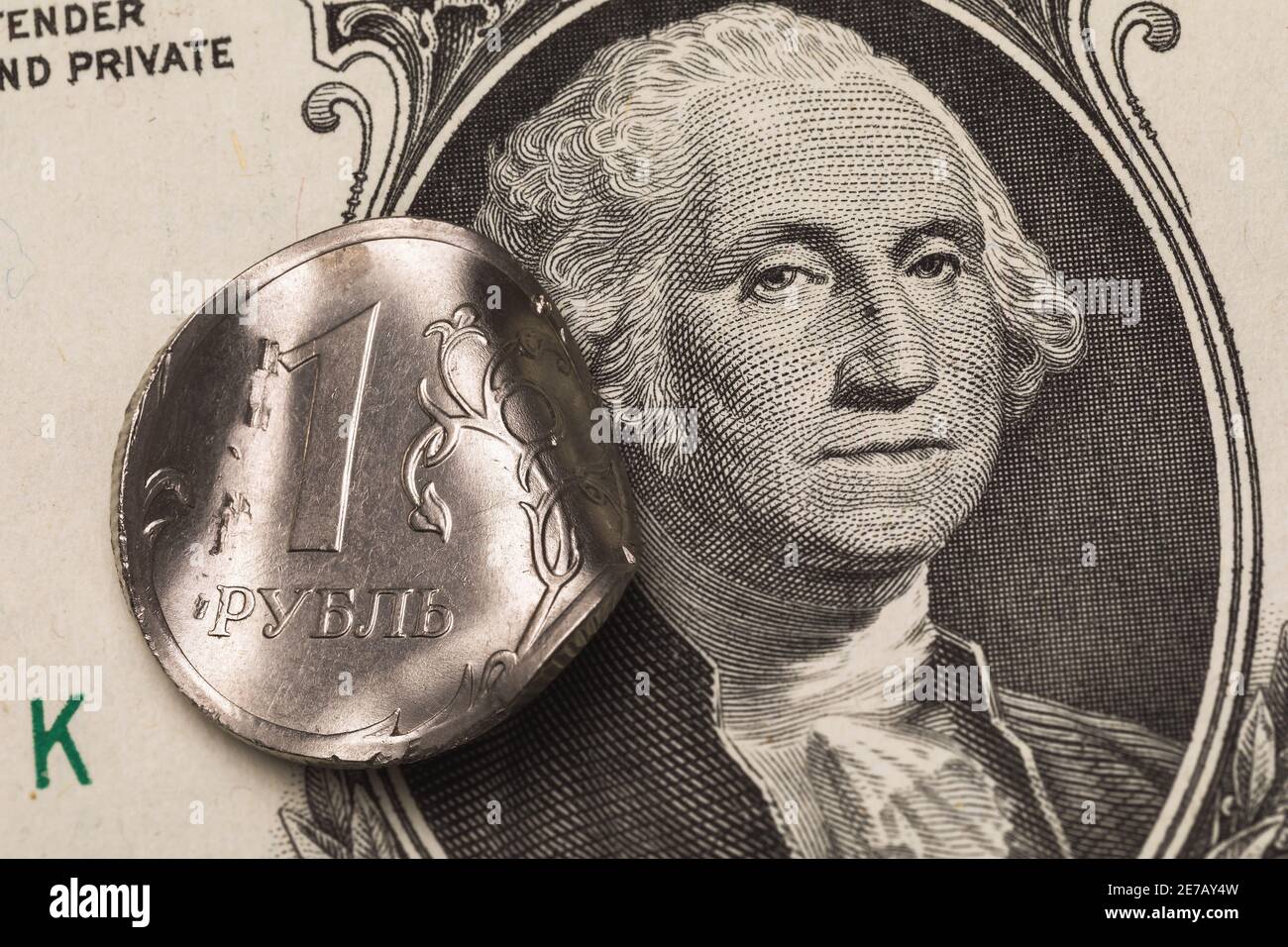 Deformierte Münze ein Rubel auf dem Hintergrund der Dollar-Banknote, Nahaufnahme. Auf der Münze die Inschrift in russischen Buchstaben Rubel. Stockfoto
