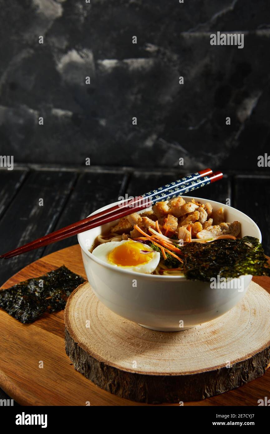 Japanische Ramen-Suppe mit Huhn, Ei, Knoblauch und Nudeln auf dunklem Holzgrund. Asiatische Miso Ramen Nudeln. Stockfoto
