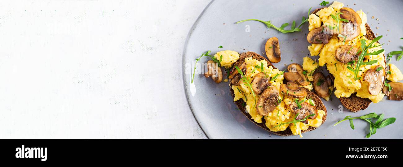 Rührei und gebratene Pilze auf Brot. Hausgemachtes Frühstück oder Brunchmenü - Rühreier und Pilze Sandwiches. Draufsicht, Banner, Kopierbereich Stockfoto