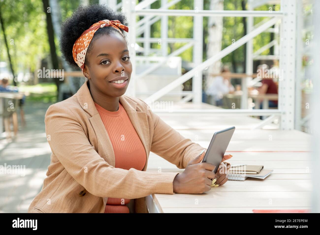 Porträt einer afrikanisch lächelnden Frau beim Sitzen in der Kamera Der Tisch im Café und mit dem digitalen Tablet Stockfoto
