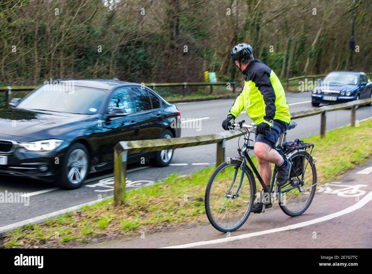 Ein Erwachsener Mann Radfahren auf einem Radweg Blick auf den Verkehr, wie er versucht, die Hauptstraße wieder zu verbinden. Der Radfahrer trägt eine gut sichtbare Jacke und einen Helm. Stockfoto