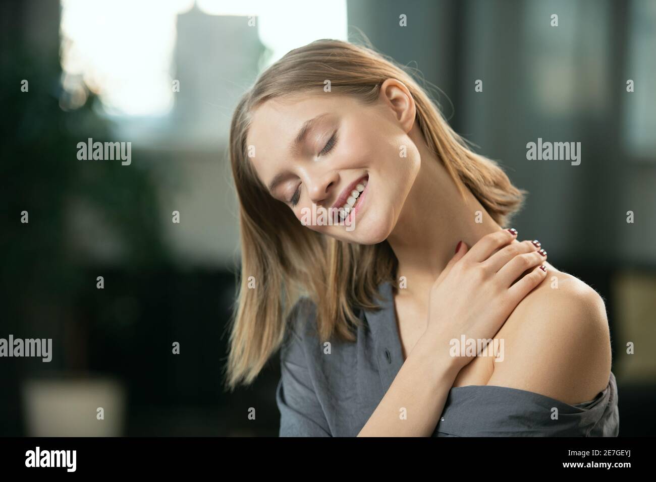 Junge blonde Frau mit toothy Lächeln Anwendung natürliche handgemachte Kosmetik Produkt auf ihrem Hals und Körper und genießen es in Am Morgen Stockfoto