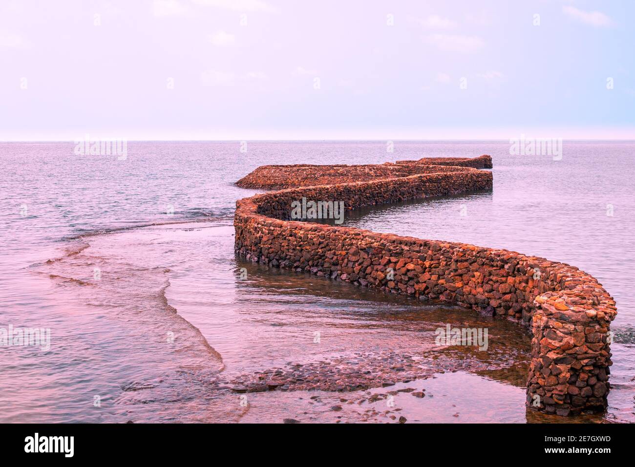 Die Steininstallation in Form einer kurvenreichen Linie geht ins Meer, lila Tönung. Ruhige Meereslandschaft. Rest in Asien. Stockfoto