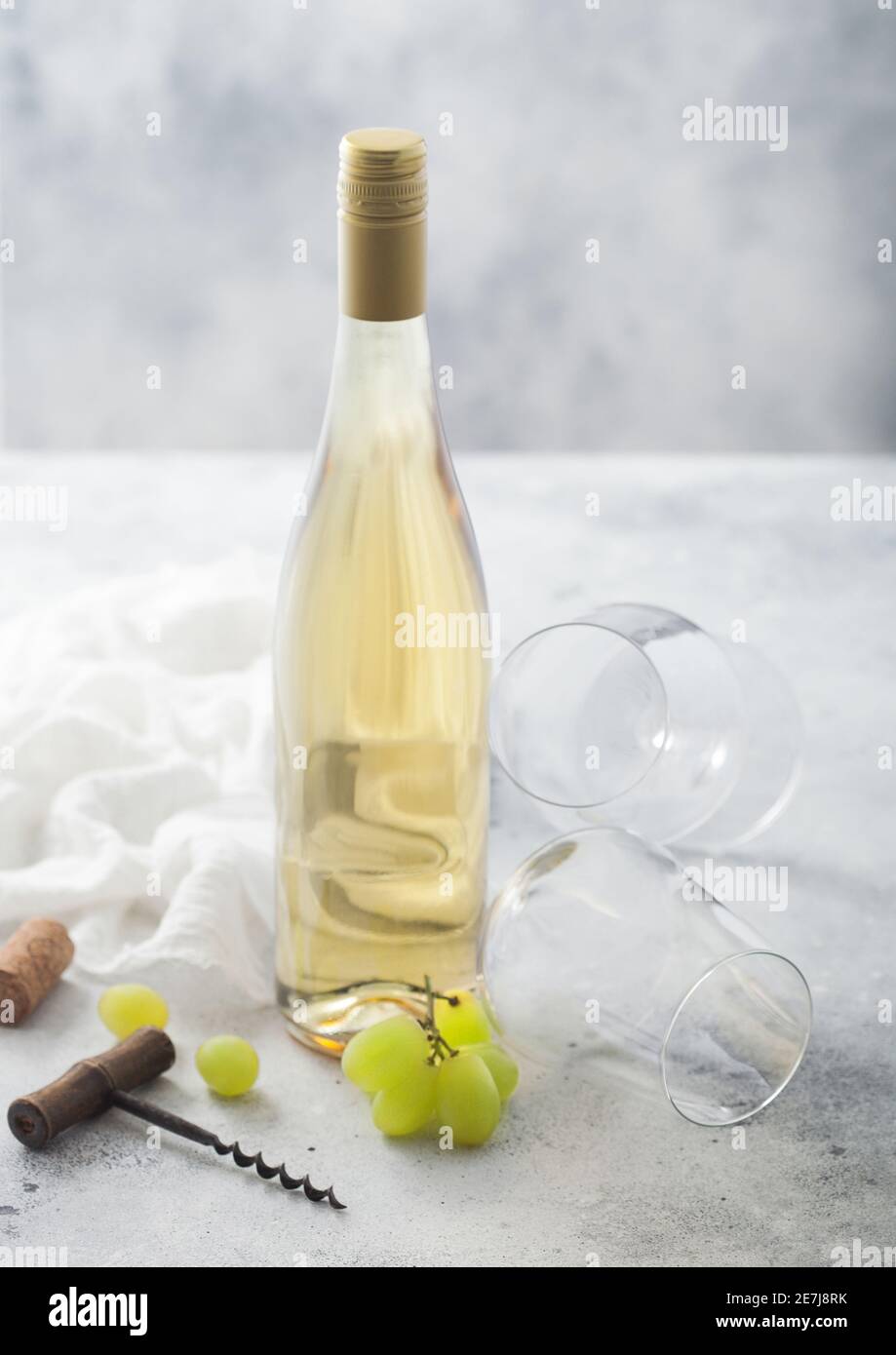 Leere Gläser und eine Flasche Sommer Weißwein mit Trauben, Korken und Korkenzieher auf hellem Tischhintergrund. Stockfoto