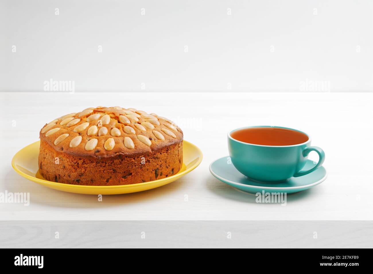 Hausgemachter Kuchen mit Mandeln und einer Tasse Tee auf einem weißen Holztisch. Copyspace. Stockfoto