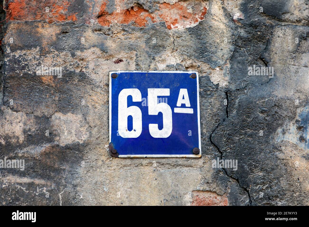 Nummer 65, die Anzahl der Häuser, Wohnungen, Straßen. Die weiße Zahl auf der blauen Metallplatte, die Hausnummer fünfundsechzig (65) auf der rauen Wand. Stockfoto