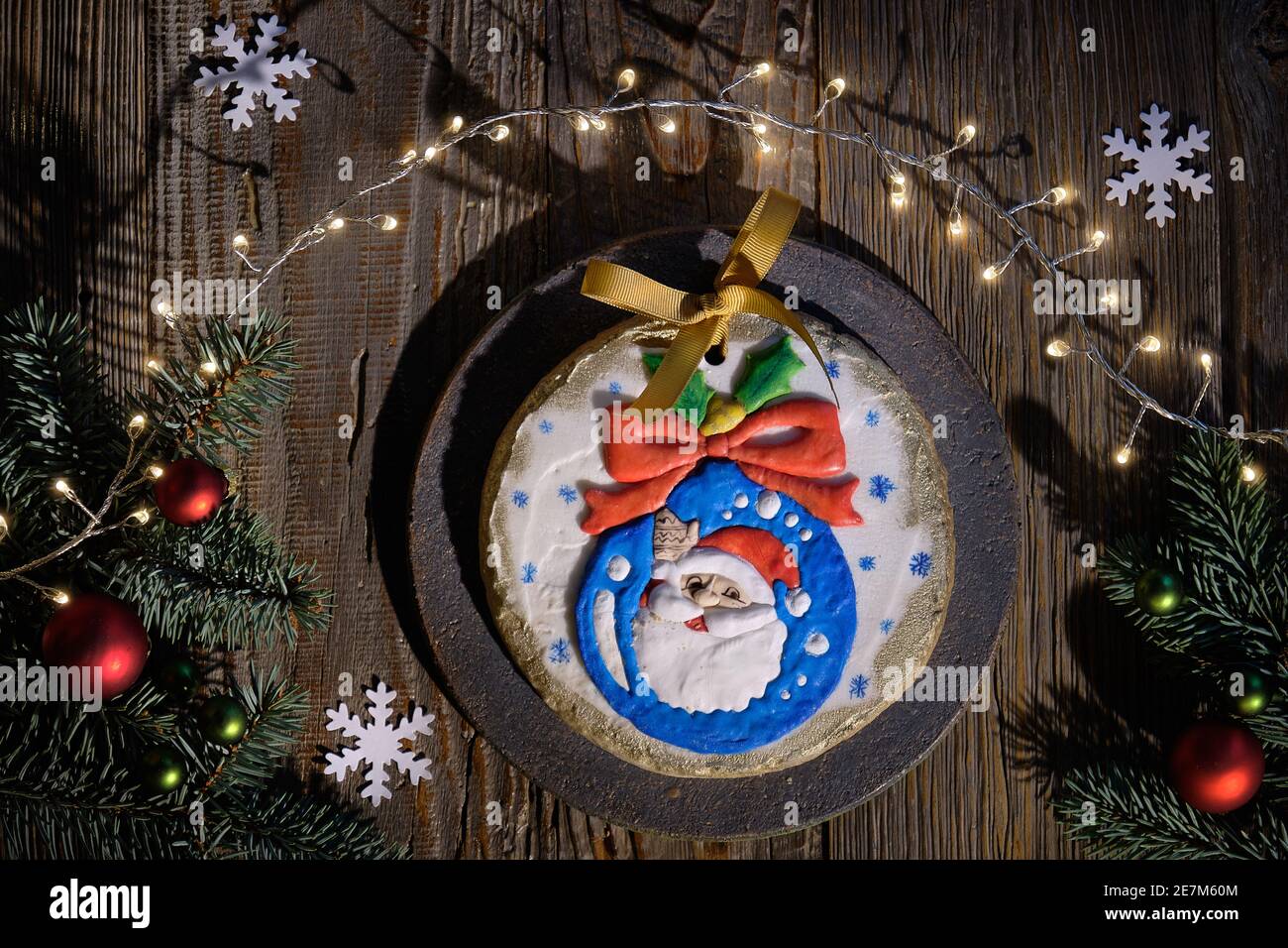Verzierte Lebkuchen mit Weihnachtsmann lächelnd aus Weihnachtskugel dekoriert. Zwei Cartoon-Kuh-Charaktere. Weihnachten flach legen mit Tannenzweigen, roten Kugeln, Papier Stockfoto