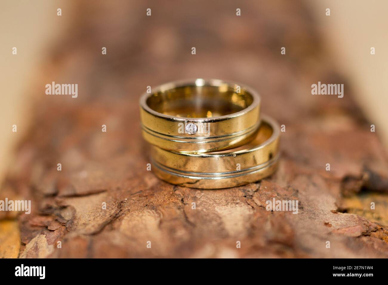 Eheringe – Nahaufnahme zweier goldener Eheringe auf einer strukturierten Holzoberfläche, die Liebe, Engagement und zeitlose Eleganz symbolisieren. Stockfoto