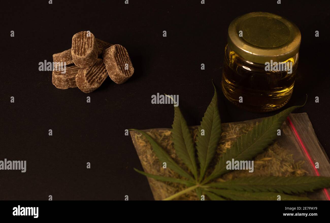 Schokolade, ein Glas voller cbd-Öl und ein Cannabisblatt auf einer Tüte mit gemahlenem Unkraut. Das Bild zeigt die Beziehung zwischen Nahrung und Cannabis Stockfoto