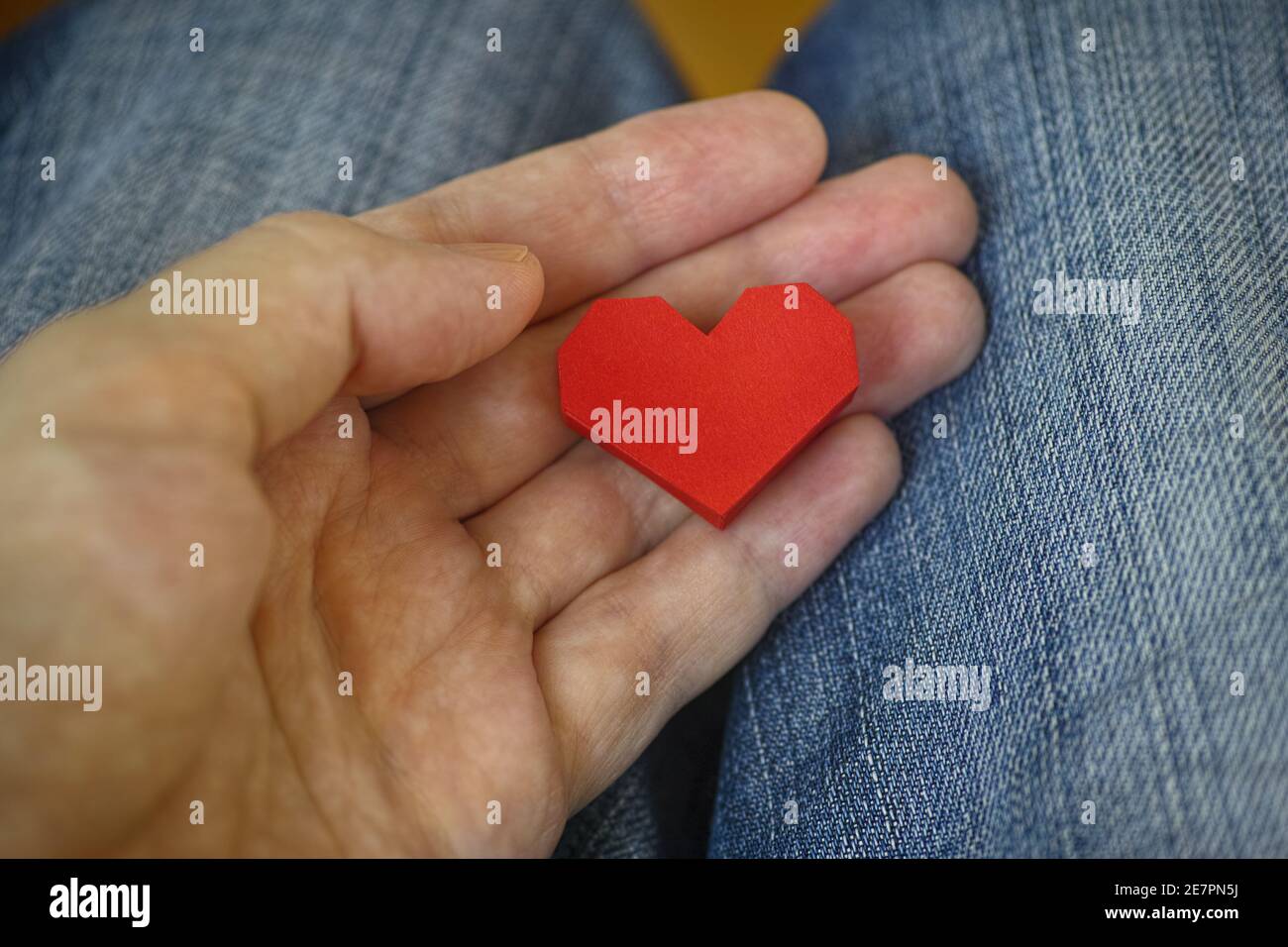 Mann hält ein rotes Origami-Herz in seiner Handfläche. Nahaufnahme. Stockfoto