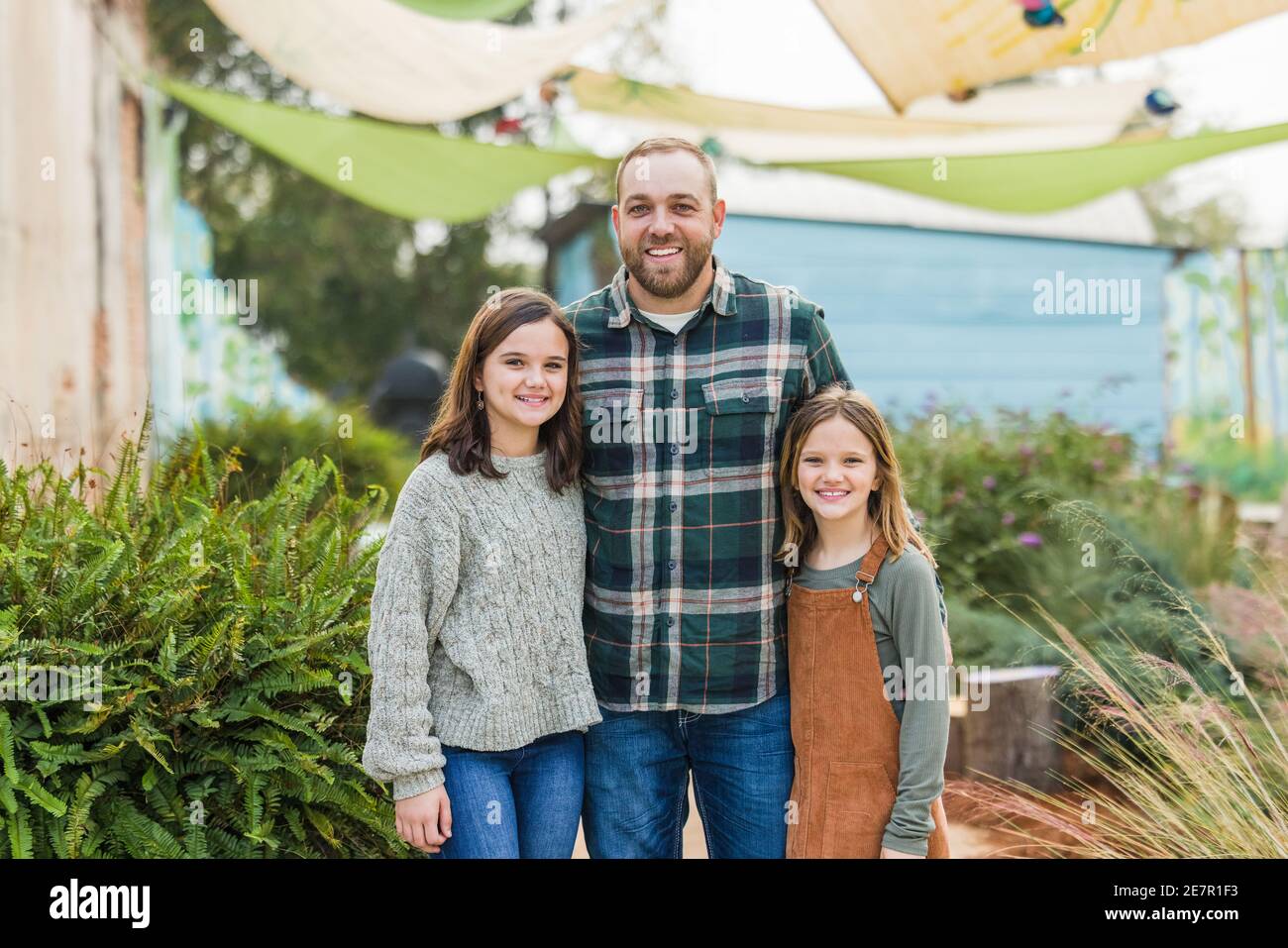 Ein Stiefvater mit seinen zwei Stieftöchtern, die draußen im Haus stehen Ein Park in der Innenstadt Stockfoto