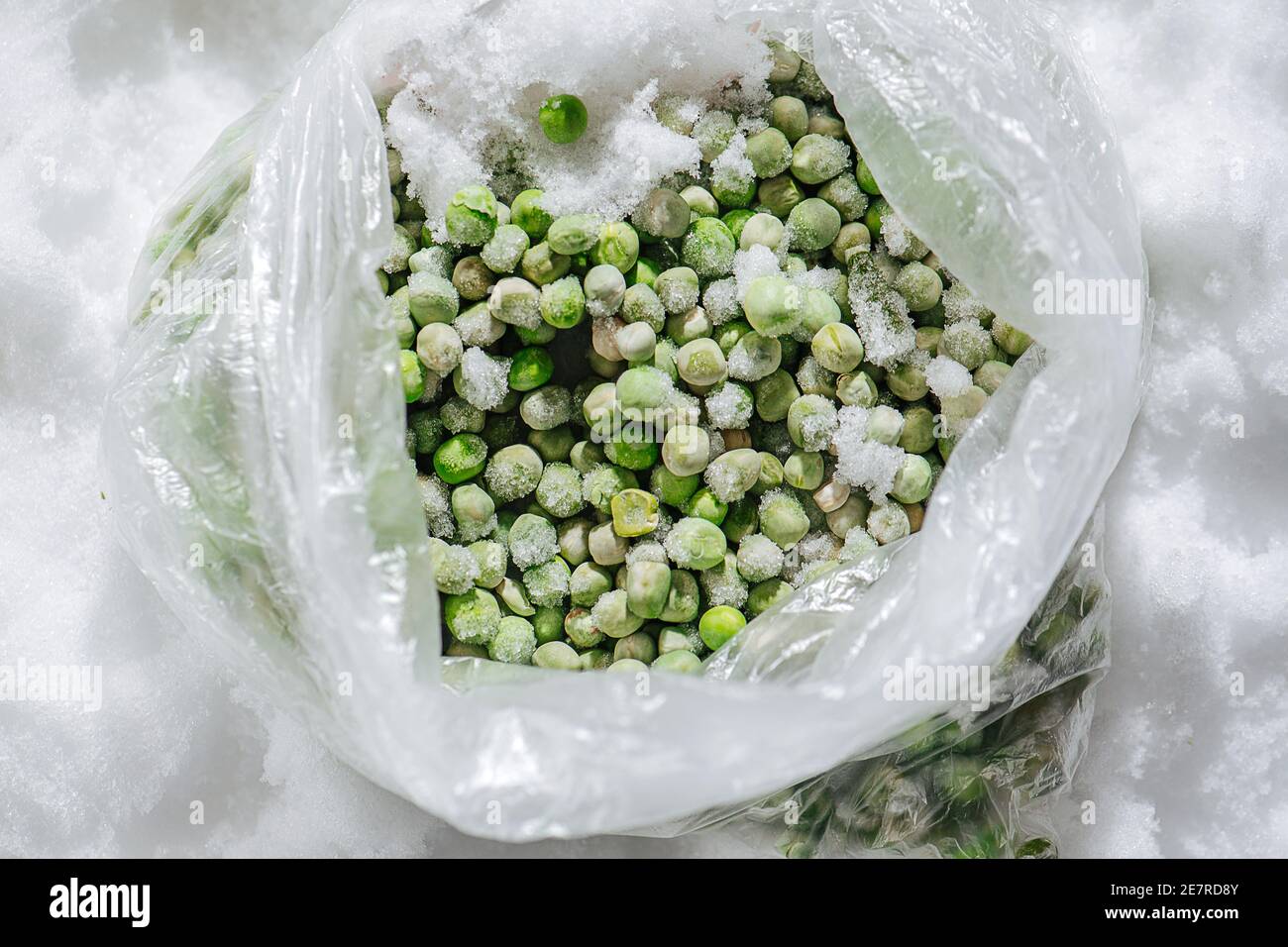 Grüne gefrorene Erbsen, bedeckt mit winzigen Eiskristallen in einem Plastikbeutel. Draufsicht. Stockfoto