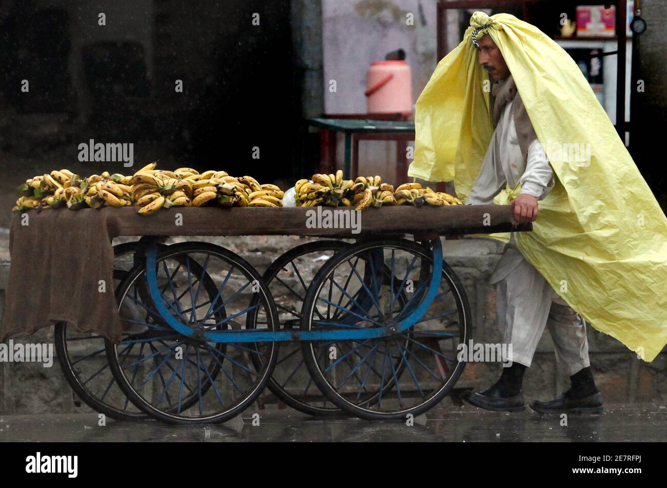 Ein Mann wandelt eine Plane in einen Poncho um, um sich vor dem Regen zu schützen, während er Bananen entlang der Straßen von Rawalpindi am 8. Februar 2010 verkauft. Schnee und Regen fielen über Kaschmir und Punjab, die Provinzen Nordwest-Grenze und Balochistan, sagte die meteorologische Abteilung Pakistans auf ihrer Website. REUTERS/Faisal Mahmood (PAKISTAN - Tags: UMWELT LANDWIRTSCHAFT GESCHÄFT) Stockfoto