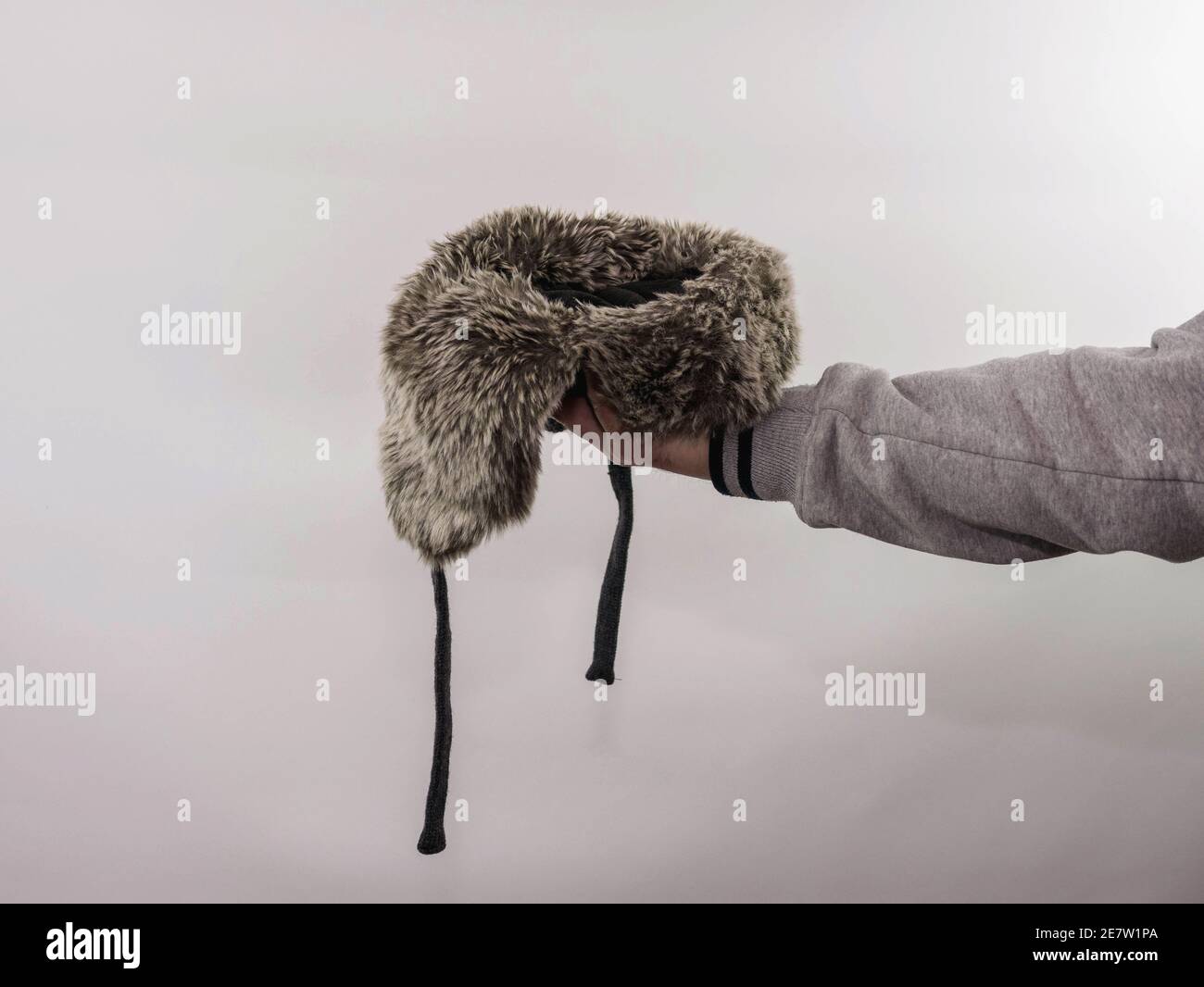 Ein Obdachloser bittet um Geld, hält einen Hut in der Hand auf einem weißen Hintergrund, einen Ort, um ein Produkt in einen Hut mit Ohrenklappen, ein Mann bittet um Mo Stockfoto