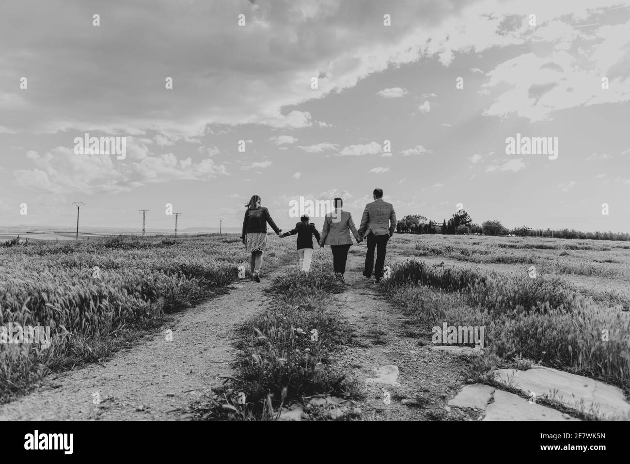 Graustufenaufnahme einer jungen Familie, die durch das Feld geht An einem bewölkten Tag Stockfoto