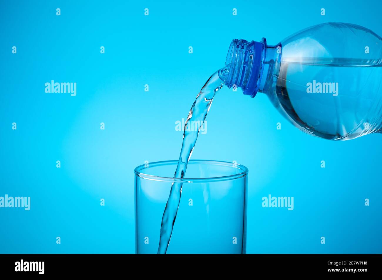 In ein leeres Glas gießen Sie frisches Wasser auf einen blauen Hintergrund. Stockfoto