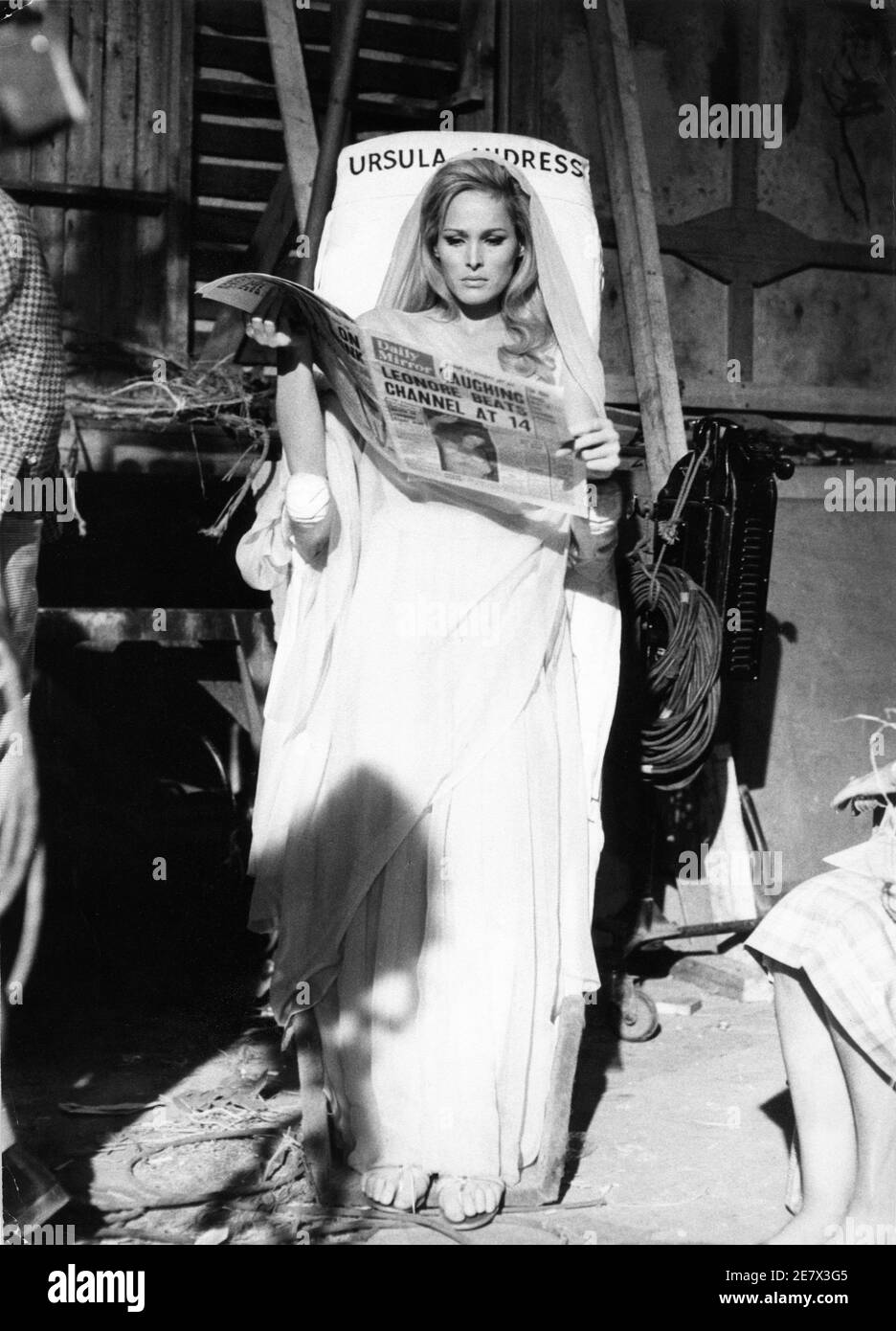 URSULA ANDRESS in Kostüm als Ayesha Daily Mirror Zeitung liest während der Pause auf Costume Board bei Dreharbeiten ZU SHE 1965 Regisseur ROBERT DAY nach dem Roman von H. Rider Haggard Hammer Films / Warner - Pathe Distributors Stockfoto