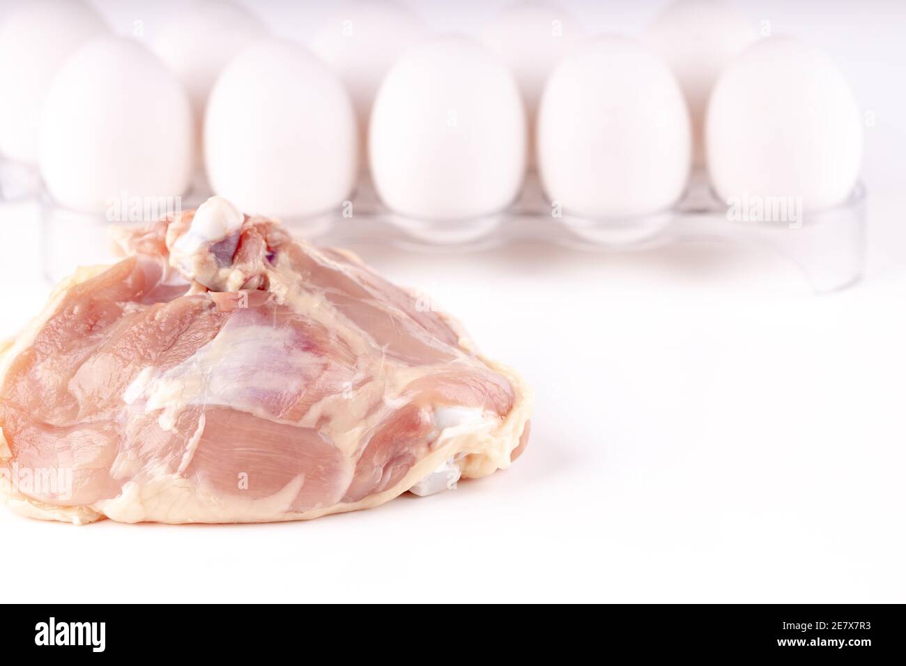 Rohes Hühnerfleisch und Gruppe von Eiern dahinter auf weißem Hintergrund. Copy Space. Chicken Industrie Konzept Stockfoto