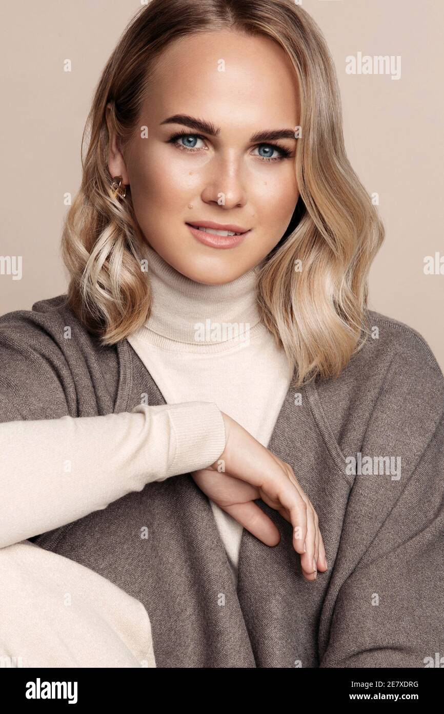 Schöne junge Frau mit blonden welligen Haaren tragen Poncho suchen Im Studio mit einem Lächeln vor der Kamera Stockfoto