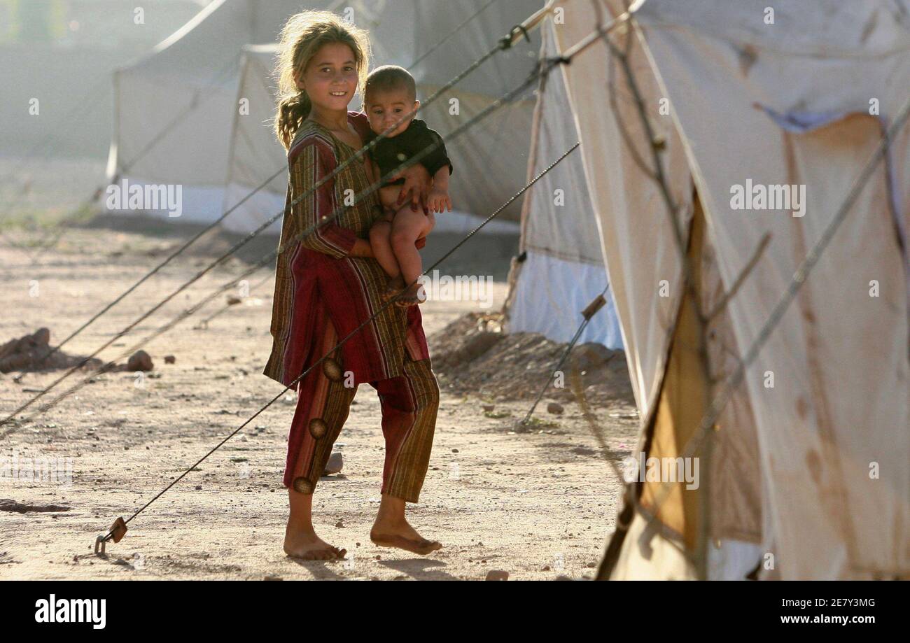 Eine Vertriebene Mädchen auf der Flucht einer Militäroffensive in der Swat-Tal-Region hält ihre Geschwister außerhalb ihrer Familienzelt der UNHCR (UNO-Hochkommissariat für Flüchtlinge) Jalozai Camp, etwa 140 km (87 Meilen) Nord-westlich von der pakistanischen Hauptstadt Islamabad 24. Mai 2009. Pakistanische Flugzeuge Taliban-Kämpfer am Sonntag in der Region Orakzai ethnischen Pashtun bombardierten töten mindestens sieben, während Soldaten gekämpft Aufständischen in den Hauptort der SWAT-Region, sagte Regierungsbeamte. REUTERS/Faisal Mahmood (PAKISTAN Gesellschaft Konflikt Politik) Stockfoto