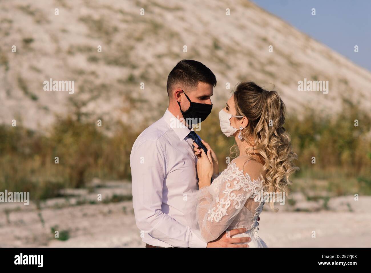 Junge liebende Paar in medizinischen Masken im Park während der Quarantäne an ihrem Hochzeitstag zu Fuß. Stockfoto