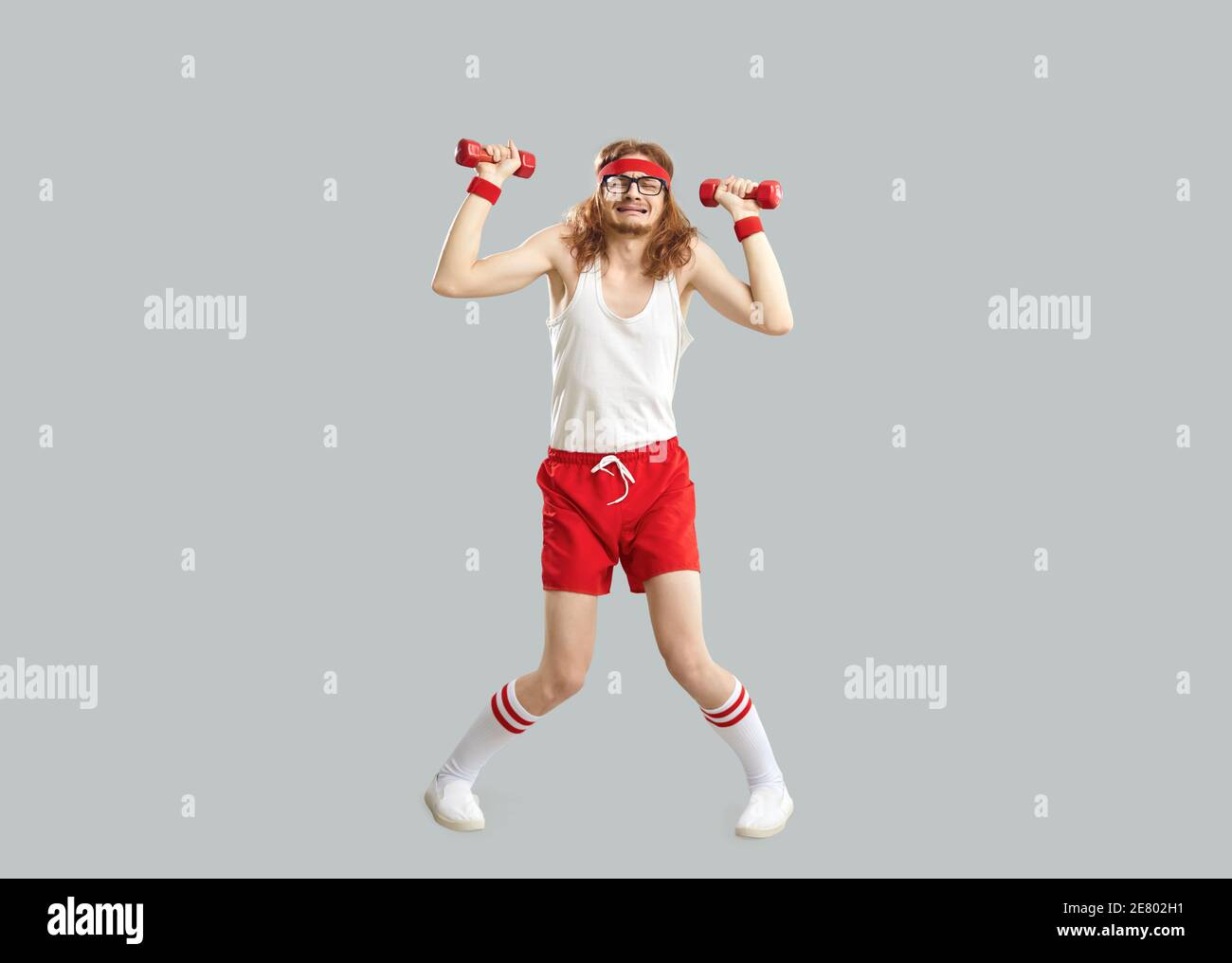 Lustige müde dünne Mann tun Übung mit Turnhalle Hanteln isoliert Auf grauem Hintergrund Stockfoto