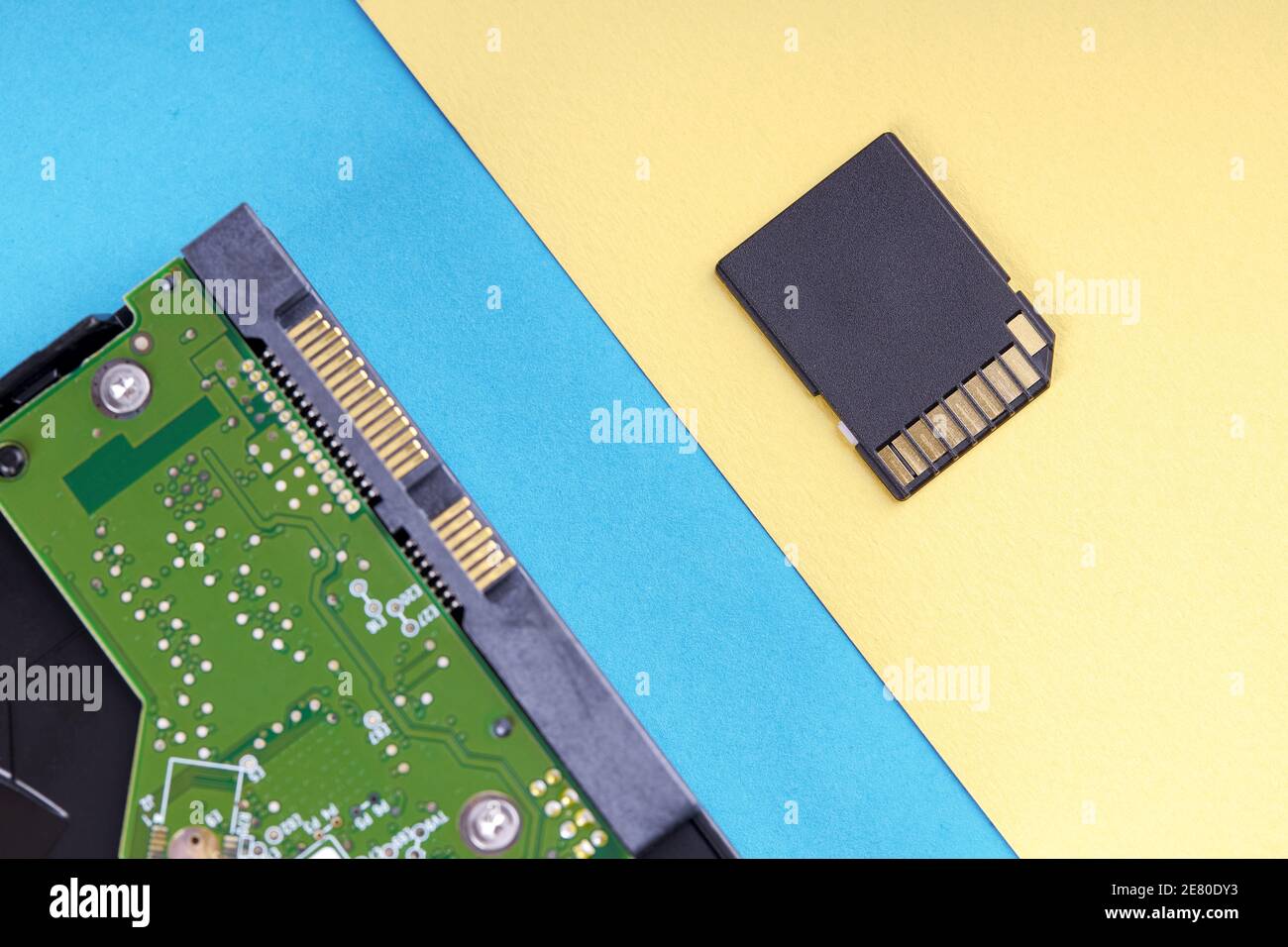 Desktop-pc-Festplatte oder festplatte auf blauem Hintergrund und kleine schwarze sd-Speicherkarte auf hellgelben Hintergrund. Pastellfarben Stockfoto