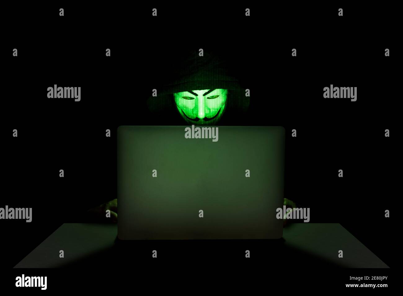 Mitglied der anonymen Hacker-Gruppe, die eine Maske vor seinem Laptop trägt, während sie einen Hack begeht. Stockfoto